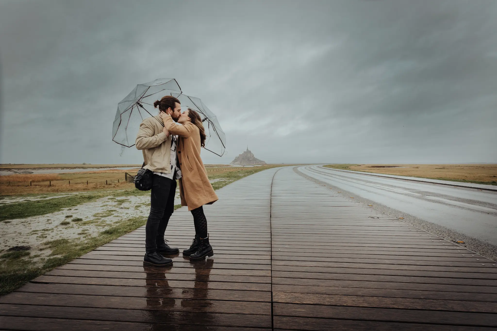 Couple kissing on the causeway of Mont Saint-Michel with the monument in the background — engagement photography