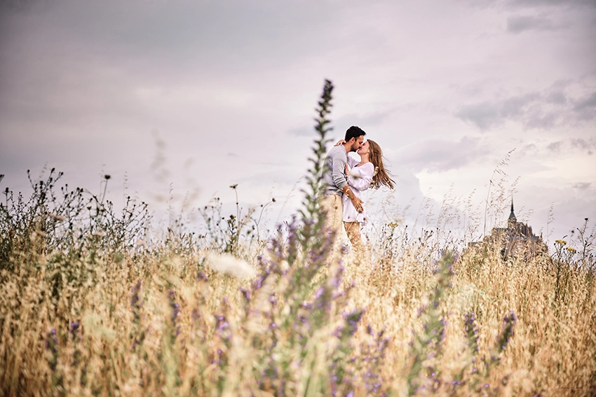 Couple kissing in the wild meadows of Mont Saint-Michel after the marriage proposal — engagement photography Normandy