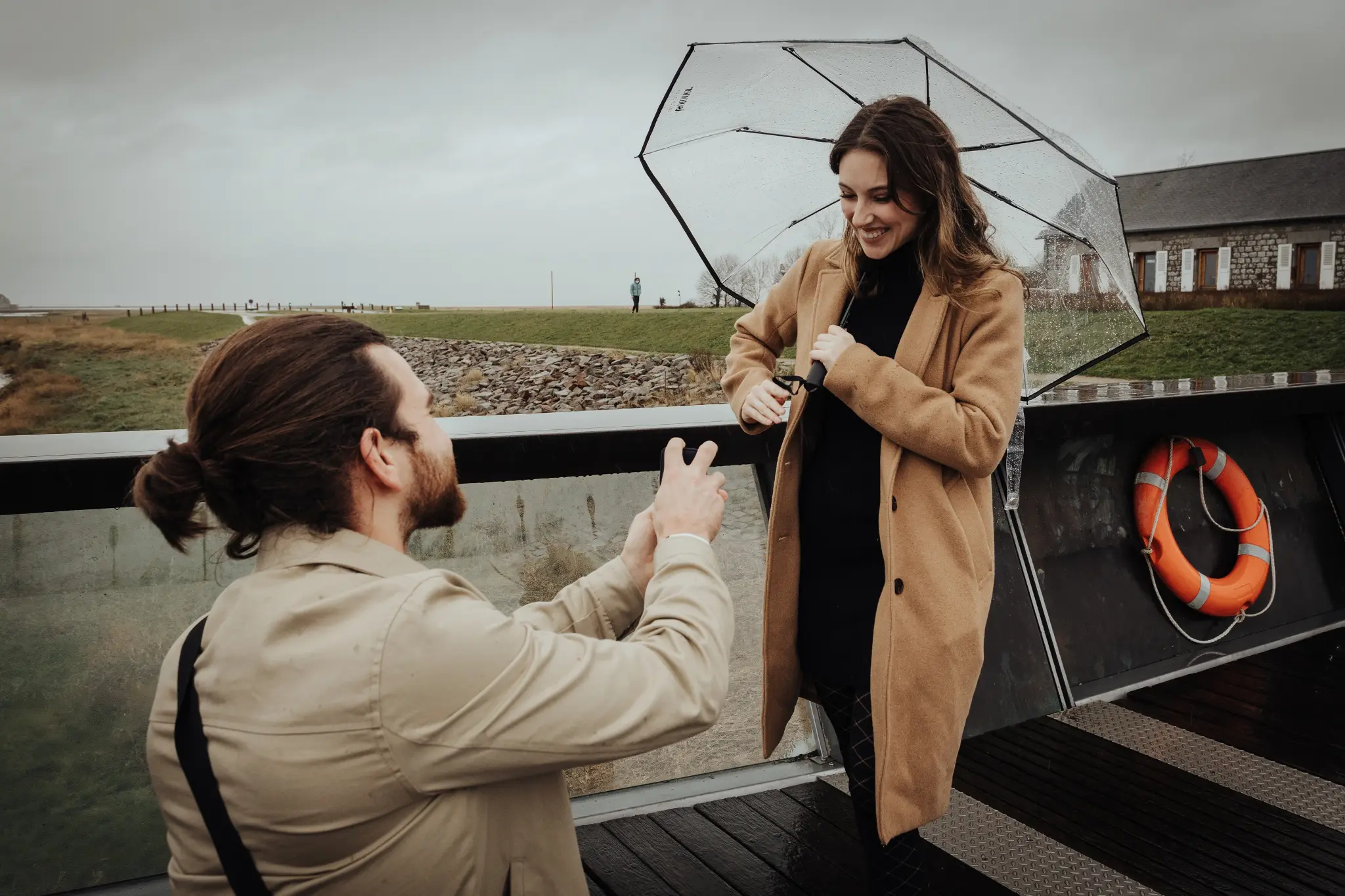Man on one knee proposing on the bridge of Mont Saint-Michel in the rain — surprise proposal photographer France