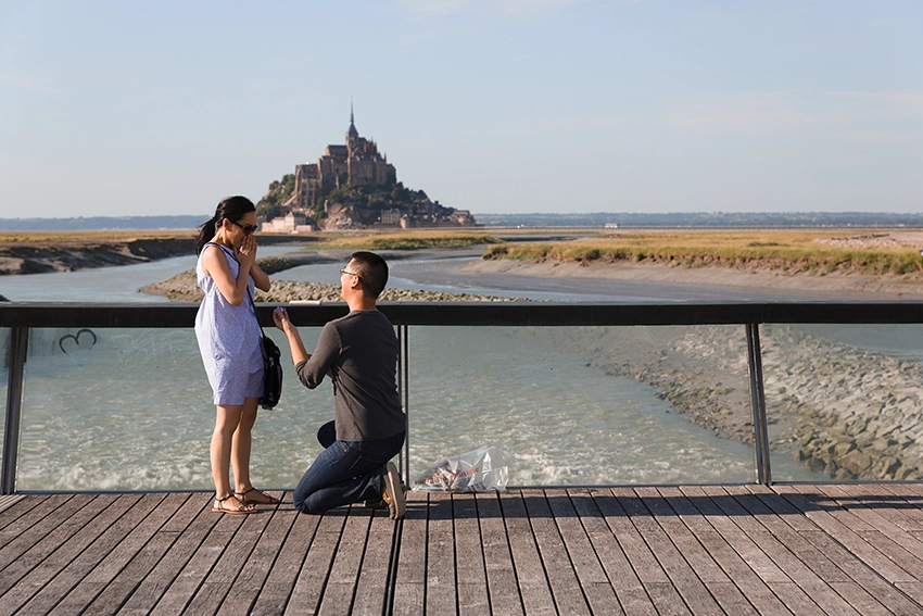 Marriage proposal at Mont Saint-Michel — man on one knee offering the engagement ring on the bridge, proposal photographer Normandy